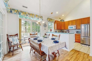 A kitchen with wooden cabinets, a stainless steel refrigerator, and a dining area with a table set for four. - Bear Trap Dunes townhouse w/shared pool, tennis, fitness center, on-site golf (Ocean View)