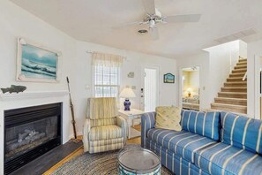 Ein Wohnzimmer mit Kamin, einem gestreiften Sessel, einem blau gestreiften Sofa und einem Deckenventilator.