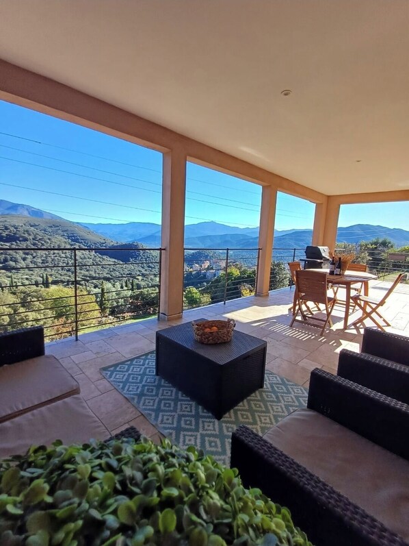 Ein Balkon mit Blick auf Berge, einem Tisch mit Stühlen und einem Obstkorb.