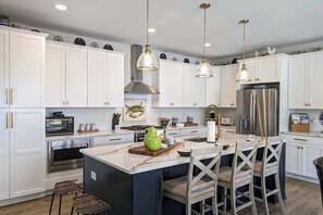 A modern kitchen with white cabinets, stainless steel appliances, and a central island with bar stools. - Town of Bethany Beach house w/private pool, hot tub, games, deck, grill (Bethany Beach)