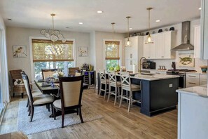 A modern kitchen with a central island, pendant lighting, and a dining area with chairs and a table. - Town of Bethany Beach house w/private pool, hot tub, games, deck, grill (Bethany Beach)