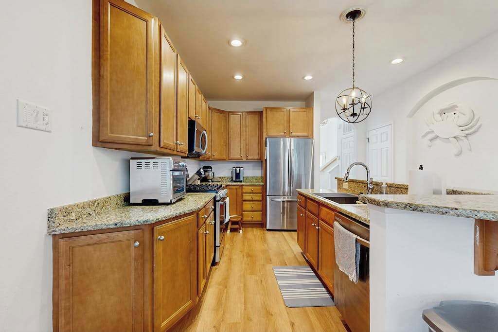 A kitchen with wooden cabinets, stainless steel appliances, granite countertops, and a hanging light fixture.