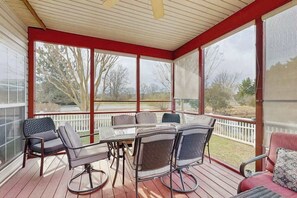 Uma área externa coberta com mesa, cadeiras, janelas amplas e vista para o exterior.