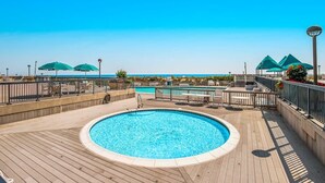 Area piscina con un molo di legno, una piscina circolare e ombrelloni verdi.