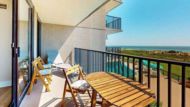 Un balcone con tavolo e sedie in legno, una piscina e vista sulla spiaggia.