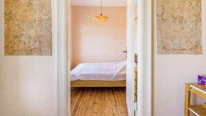Un pasillo estrecho que conduce a un dormitorio con cama, suelo de madera y una lámpara colgante.