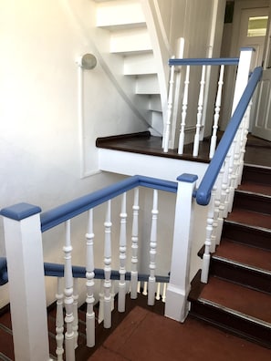 Eine Treppe mit weißen Balustraden und blauen Handläufen, die zu einem Zwischenpodest mit einer Tür führt.