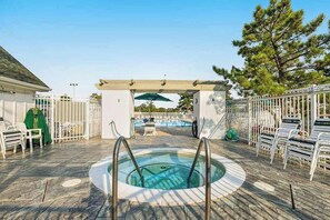 Un área de piscina con jacuzzi, sillas de descanso y una pérgola.