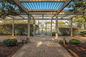 Un espacio al aire libre cubierto con una estructura de pérgola, un camino empedrado y abundante vegetación.