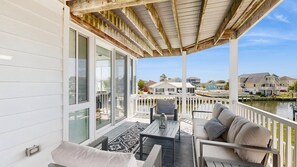 A covered balcony with a seating area, large windows, and a view of a body of water and other buildings. - Keen-Wik on the Bay bay front home w/private pool & hot tub (Selbyville)