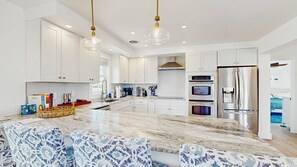 A modern kitchen with white cabinets, stainless steel appliances, a marble island, and patterned blue and white chairs. - Keen-Wik on the Bay bay front home w/private pool & hot tub (Selbyville)