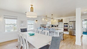 A modern kitchen with white cabinetry, stainless steel appliances, and a dining area with a white table and patterned chairs. - Keen-Wik on the Bay bay front home w/private pool & hot tub (Selbyville)