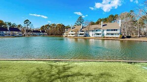A lakeside hotel with multiple buildings, a grassy area in the foreground, and trees in the background.