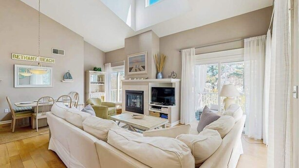 A modern living room with a sofa, TV, fireplace, and a sign reading 'BETHANY BEACH'.