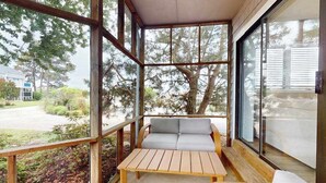 Une terrasse en bois avec un canapé et une table, de grandes fenêtres et une vue sur les arbres et une route.