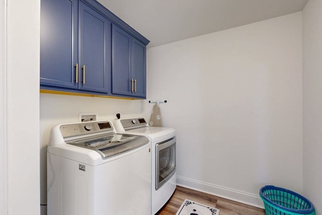 A laundry room with a washing machine and dryer, blue cabinets, and a laundry basket.