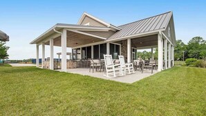 Une terrasse extérieure couverte, dotée d’une cheminée en pierre, de chaises blanches et d’une table à manger.