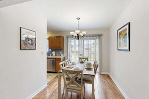A dining area with a table set for four, wooden chairs, a chandelier, and framed artwork on the walls. - Breezewood dog-friendly house w/firepit, deck, patio, grill & game room (Rehoboth Beach)