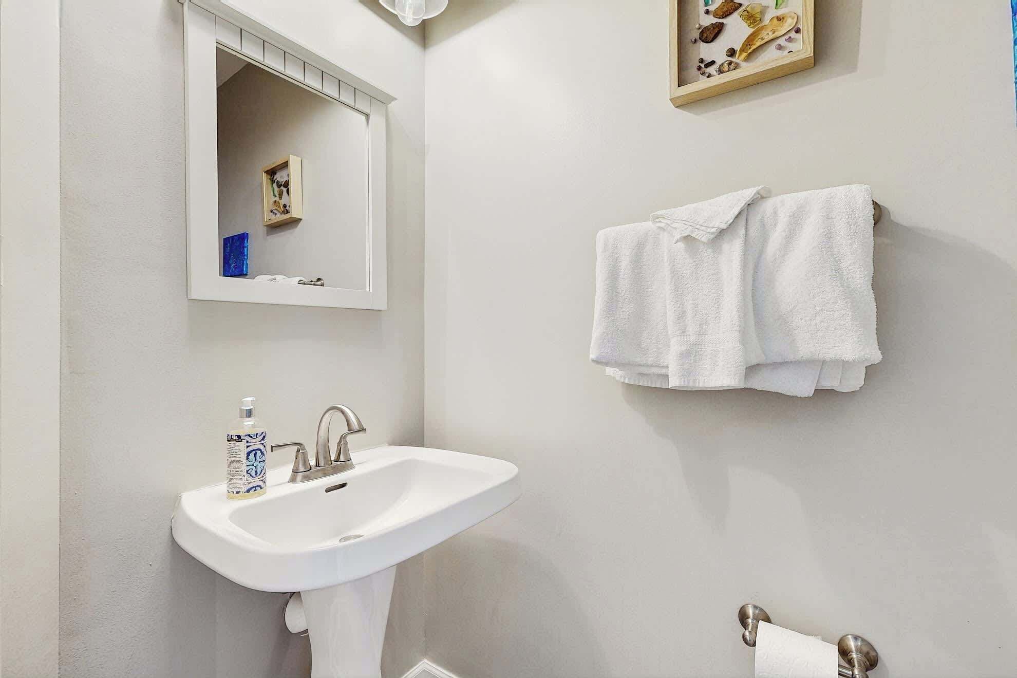 Ein Badezimmer mit einem weißen Waschbecken, einem Spiegel, einem Handtuchhalter mit zwei Handtüchern und einem gerahmten Bild an der Wand.