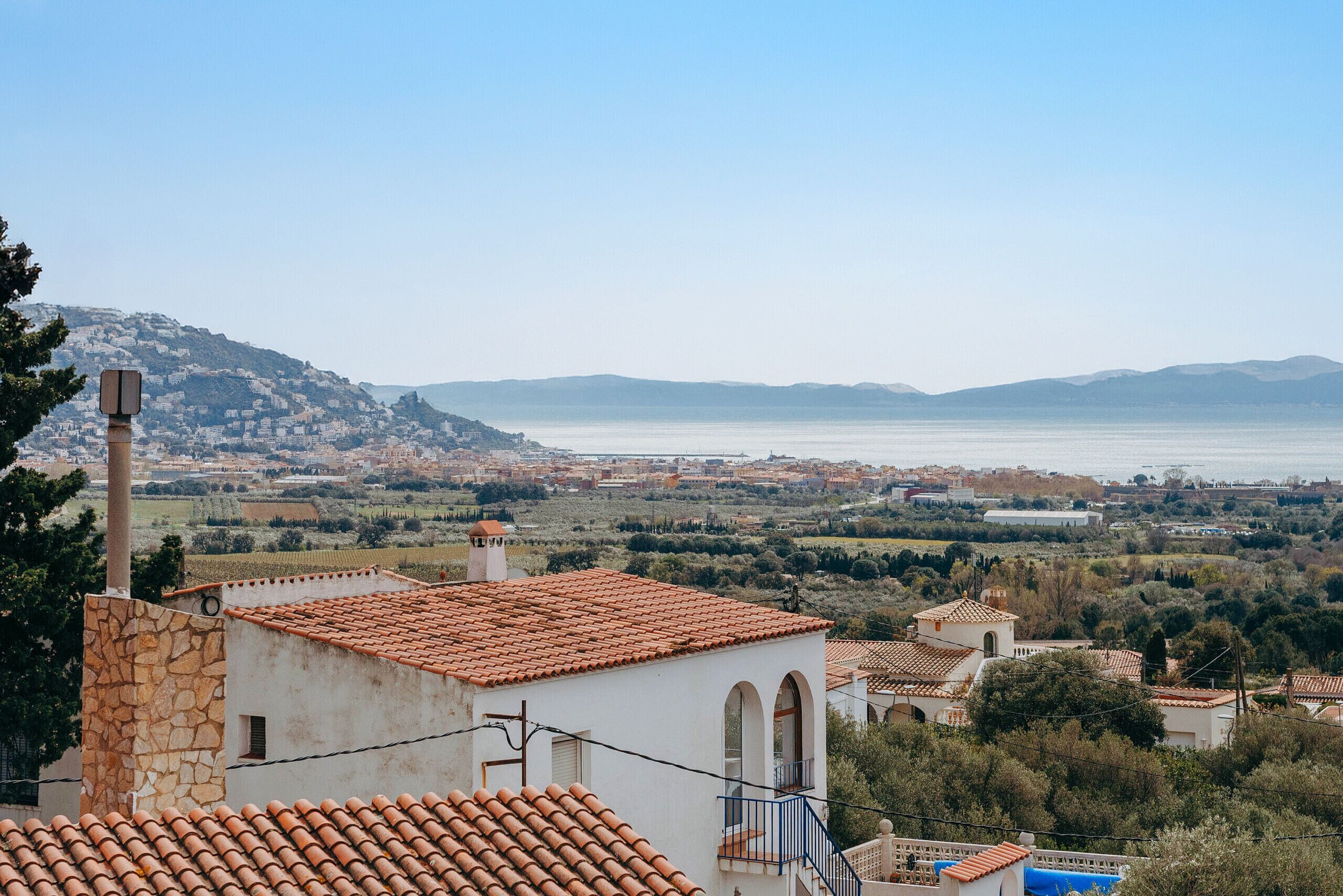 Une ville côtière aux bâtiments aux toits de tuiles rouges, avec un ciel dégagé et une vue sur la mer.