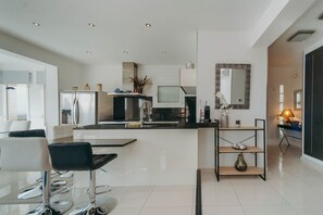 Una cocina moderna con una isla central, un comedor con taburetes de bar y un espacio de sala con sofá y mesa de centro.