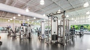 Academia com diversos equipamentos de exercício, um espelho grande e iluminação industrial no teto.
