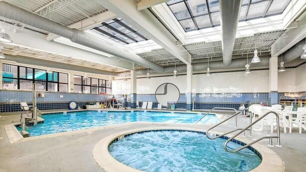 Piscina interna com hidromassagem, espreguiçadeiras e uma ampla parede envidraçada.