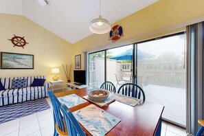 A living room with a sofa, dining table, chairs, a television, and a large window with a view. - Sea Colony - 39469 Woodland View #5303 | Condo in Bethany Beach (Bethany Beach)