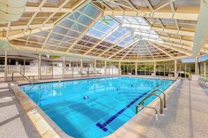 Une piscine intérieure dotée d’un toit en verre, d’une eau cristalline et d’une terrasse carrelée.