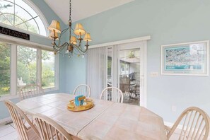 A dining area with a large table, chairs, a chandelier, and a view through a window. - Salt Pond house with golf course views, pool, tennis, fireplace, porch, deck, AC (Bethany Beach)