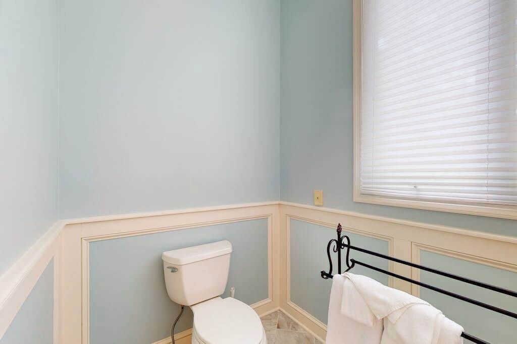 Een badkamer met een toilet, een handdoekhouder en een raam met zonwering.