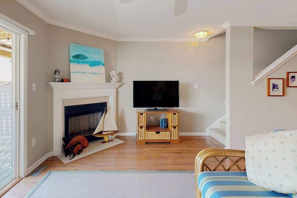 Una sala de estar con chimenea, televisor, un mueble de televisión de madera, una maqueta de velero y una escalera.