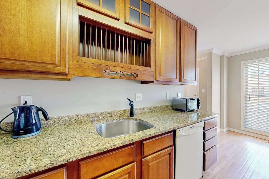 A kitchen with wooden cabinets, a granite countertop, a stainless steel sink, a kettle, and a toaster.