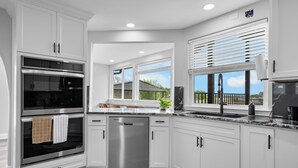 A modern kitchen with white cabinetry, stainless steel appliances, and a large window overlooking a deck. - The Lone Star Lakehouse at Eagle Mountain Lake (Azle)