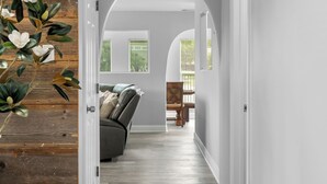 A hallway with a wooden accent wall, a framed sign above the door, and a view into a living area with a sofa and a table. - The Lone Star Lakehouse at Eagle Mountain Lake (Azle)