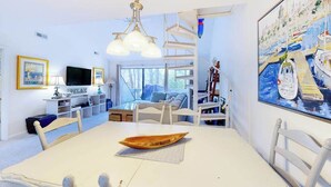 A modern living room with a white table, a TV, and a painting of a harbor. - Sea Colony home with loft, sauna, pool, tennis court, hot tub, & balcony (Bethany Beach)