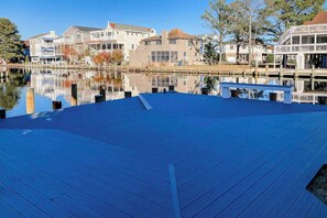 A waterfront property with a wooden deck, a calm lake, and residential buildings in the background. - Town of South Bethany enchanting canal-front retreat with decks & amazing views (Bethany Beach)