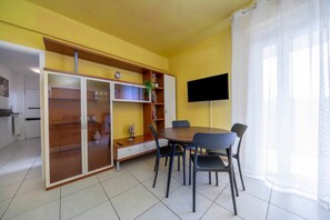 Een eetgedeelte met een tafel, stoelen, een televisie aan de muur en een grote kast met glazen deuren.