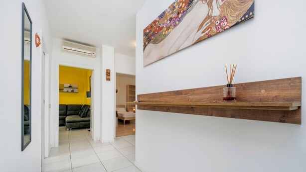 A hallway with a wooden shelf, a painting, and a yellow room in the background. - A comfortable and welcoming 60 square meters apartment, perfect for four people, located on the fourth floor of a period building without an elevator.The property is located in a quiet area, allowing our guests to easily and quickly reach the center of U (Udine)