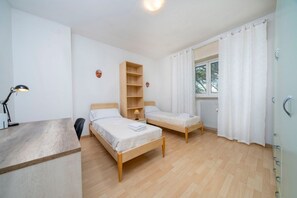 A room with two wooden beds, a desk, a lamp, a shelf, and a window with curtains. - A comfortable and welcoming 60 square meters apartment, perfect for four people, located on the fourth floor of a period building without an elevator.The property is located in a quiet area, allowing our guests to easily and quickly reach the center of U (Udine)