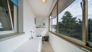 A narrow balcony with a washing machine, a small sink, and a window with a view of trees. - A comfortable and welcoming 60 square meters apartment, perfect for four people, located on the fourth floor of a period building without an elevator.The property is located in a quiet area, allowing our guests to easily and quickly reach the center of U (Udine)