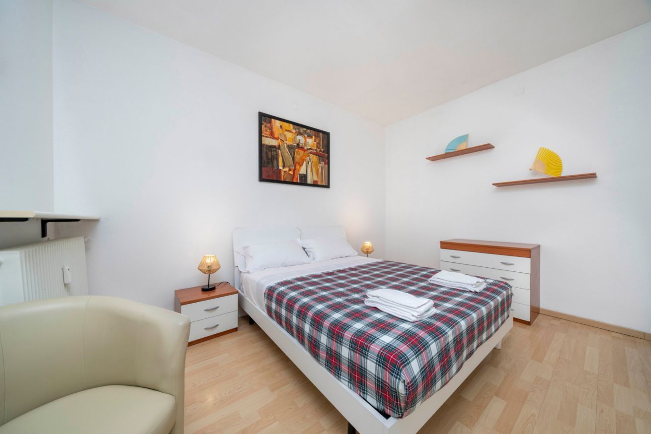 A bedroom with a bed, bedside tables, a chair, and a painting on the wall.