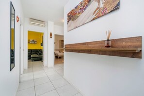 Een gang met een houten plank, een schilderij en een gele kamer op de achtergrond.