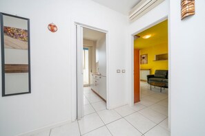 Un pasillo con una cocina, una sala de estar con sofá y mesa de centro, y una puerta que da a otra habitación.