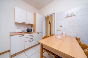 A kitchen with white cabinets, a microwave, a toaster, and a wooden dining table with chairs. - A comfortable and welcoming 60 square meters apartment, perfect for four people, located on the fourth floor of a period building without an elevator.The property is located in a quiet area, allowing our guests to easily and quickly reach the center of U (Udine)
