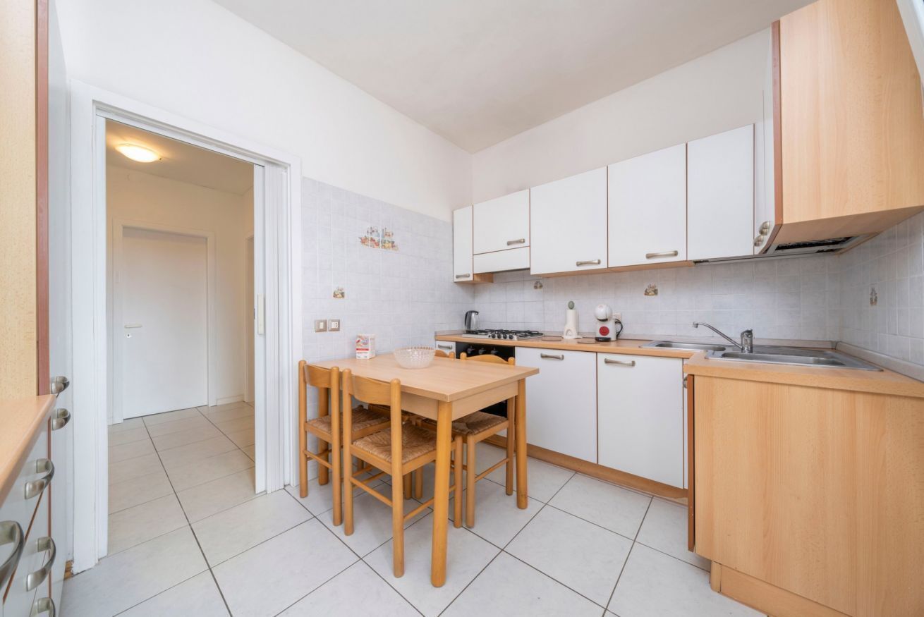 Une cuisine compacte avec des meubles blancs, une table à manger en bois et un four encastré.