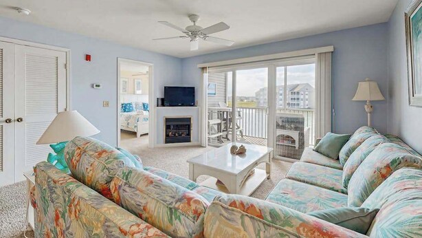 A living room with a sofa, a television, a fireplace, and a balcony with a view. - 2nd-floor Bethany Bay condo with waterfront views & on-site golf/pool/tennis (Ocean View)