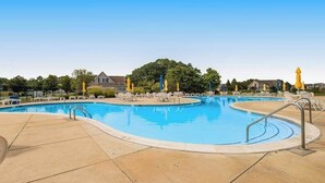 A swimming pool with lounge chairs and yellow umbrellas, surrounded by a fence and trees. - 2nd-floor Bethany Bay condo with waterfront views & on-site golf/pool/tennis (Ocean View)