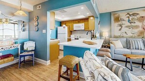 A modern kitchen with white appliances, a blue accent wall, and a dining area with a sofa and coffee table. - Sea Colony Ocean beachfront condo with 12 pools, sauna, tennis, private beach (Bethany Beach)
