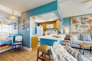 A modern kitchen with white appliances, a blue accent wall, and a dining area with a sofa and coffee table. - Sea Colony Ocean beachfront condo with 12 pools, sauna, tennis, private beach (Bethany Beach)